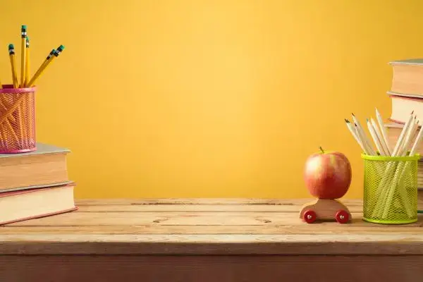 Des livres, des crayons dans un pot, une pomme rouge